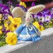 Crocheted Easter bunny in blue dress on a stone ledge with spring flowers