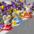 Three crocheted Easter bunnies in red, blue and orange dresses on a stone ledge with flowers