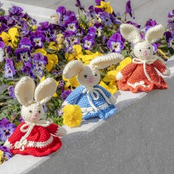 Three crocheted Easter bunnies in red, blue and orange dresses on a stone ledge with flowers