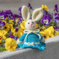 Crocheted Easter bunny in turquoise dress on a stone ledge with flowers