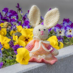 Crocheted Easter bunny in peach dress on a stone ledge with spring flowers