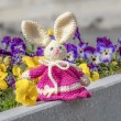Crocheted Easter bunny in bright pink dress, product photo with spring flowers