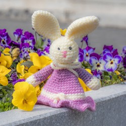 Crocheted Easter bunny in lilac dress on a stone ledge with flowers