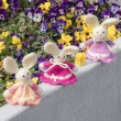 Group of crocheted Easter bunnies in different colors on a stone ledge with pansy flowers