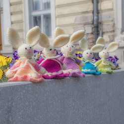 Line of crocheted Easter bunnies in multiple colors on a stone ledge, outdoor photo