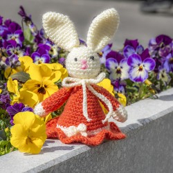 Crocheted Easter bunny in orange dress on a stone ledge with spring flowers