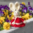 Crocheted Easter bunny in red dress on a stone ledge with flowers