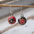 Handmade ceramic dangling earrings with red and black round beads and floral pattern, hanging on a twig