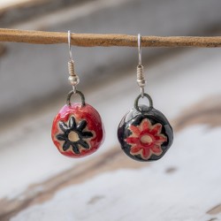 Handmade ceramic dangling earrings with red and black round beads and floral pattern, hanging on a twig