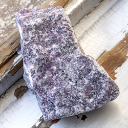 Large raw lepidolite rough stone piece in purple tones on a rustic windowsill