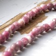 Bližnji posnetek kroglic ogrlice iz lepidolita v roza in vijoličnih tonih na leseni podlagi
