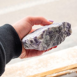 Large rough lepidolite stone held in hand, showing size and natural purple-white tones