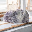 Large rough lepidolite stone piece in purple and white tones on a rustic windowsill