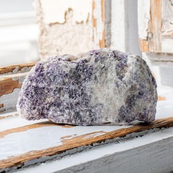 Large rough lepidolite stone piece in purple and white tones on a rustic windowsill