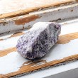 Raw lepidolite stone piece photographed from the side on a rustic painted wood surface