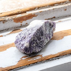 Raw lepidolite stone piece photographed from the side on a rustic painted wood surface