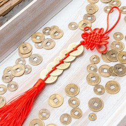 Feng shui charm with 5 Chinese coins tied with red cord and tassel on wooden tray