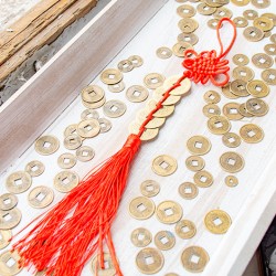 Five Chinese feng shui coins with red tassel laid out among loose Chinese-style coins