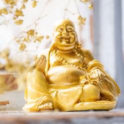 Golden yellow laughing Buddha statuette with dried flowers in background