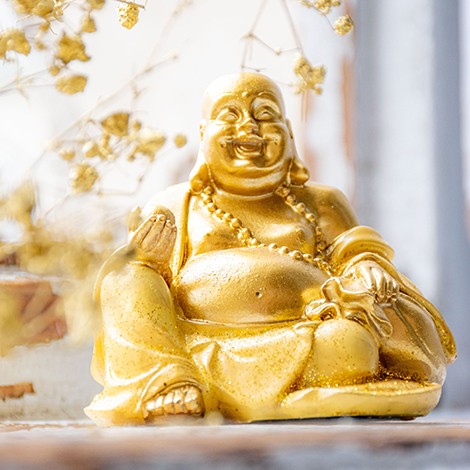 Zlato-rumen kipec smejočega Bude z nežnim ozadjem suhih rož