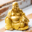Golden yellow smiling Buddha figurine on rustic wooden surface, front view