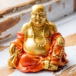 Gold-orange smiling Buddha figurine on rustic wooden surface, front view