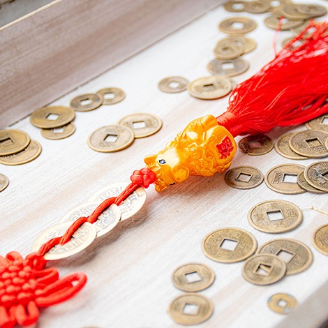 Bližnji posnetek feng shui obeska s 3 kitajskimi kovanci, zlatim Pixiu motivom in rdečim cofom