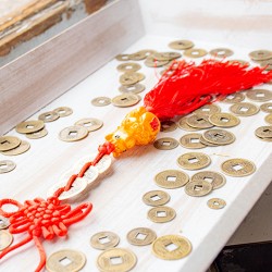 Feng shui coin charm with red tassel displayed on a wooden tray among Chinese-style coins