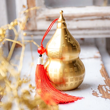 Brass Wu Lou feng shui gourd with red tassel, gold finish on rustic wood background