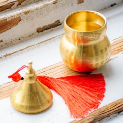 Opened brass Wu Lou gourd container with lid and red tassel on wooden surface
